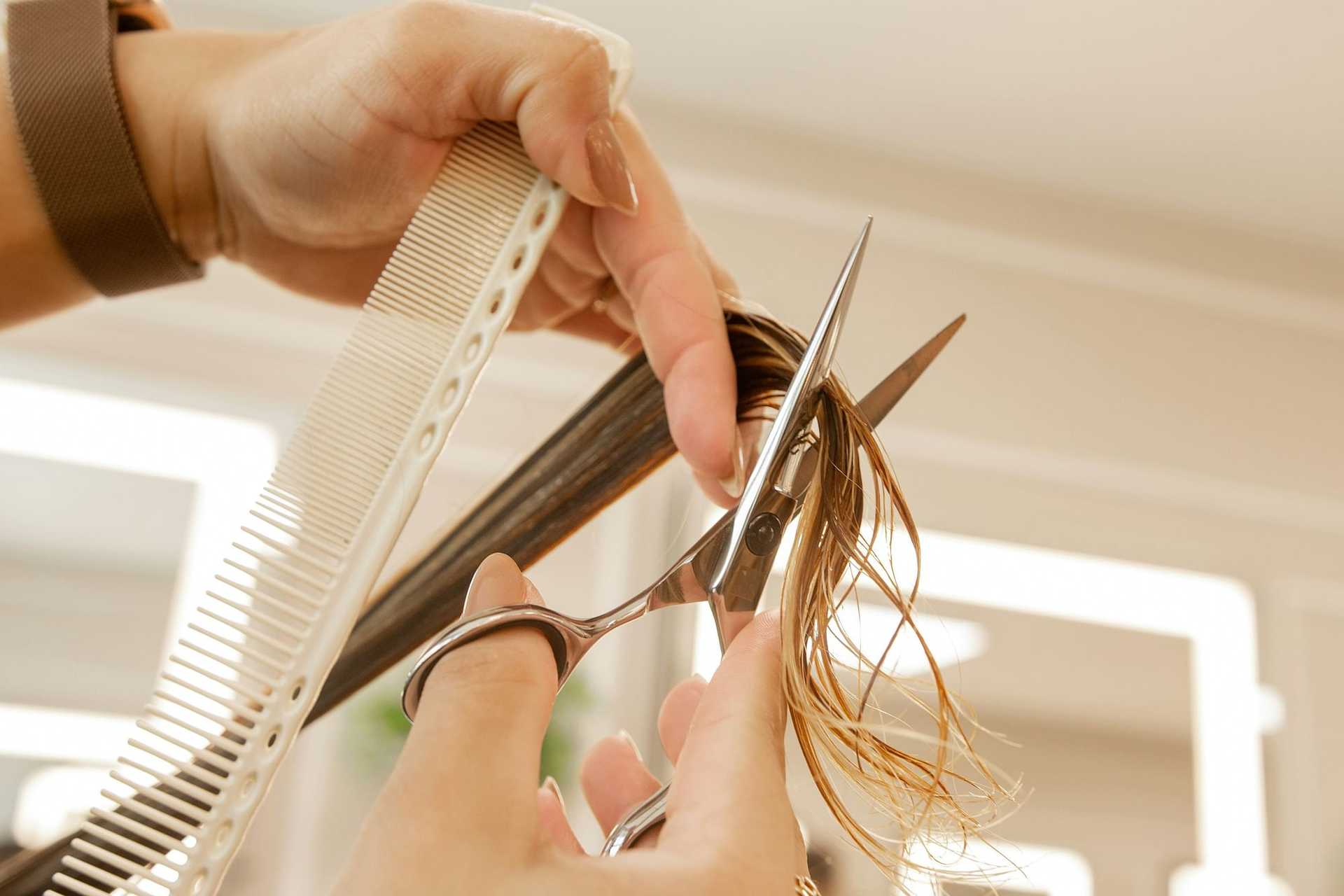 Hands cutting hair with scissors and comb in a salon setting.