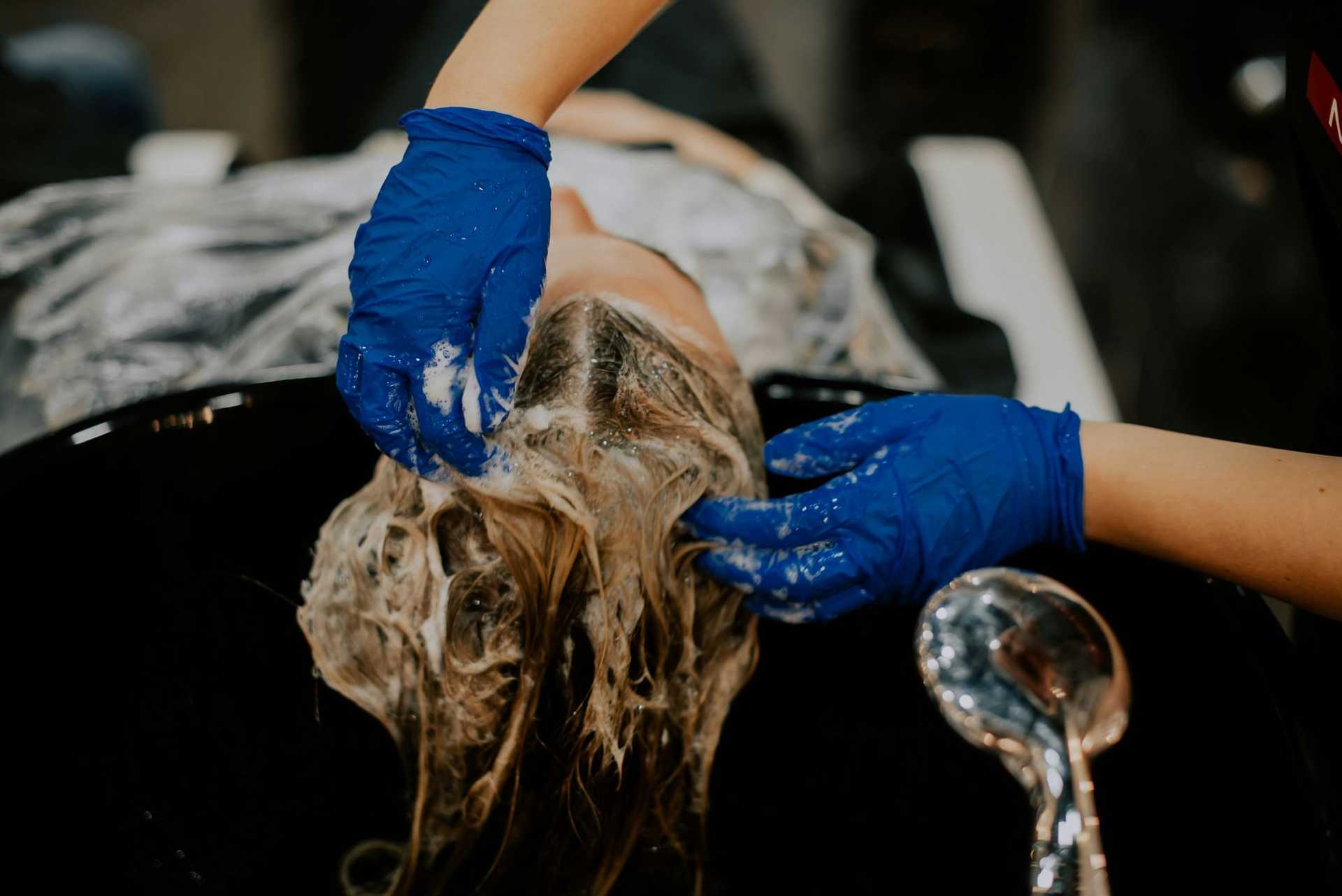 Person receiving a professional hair wash in a salon, with stylist wearing blue gloves.