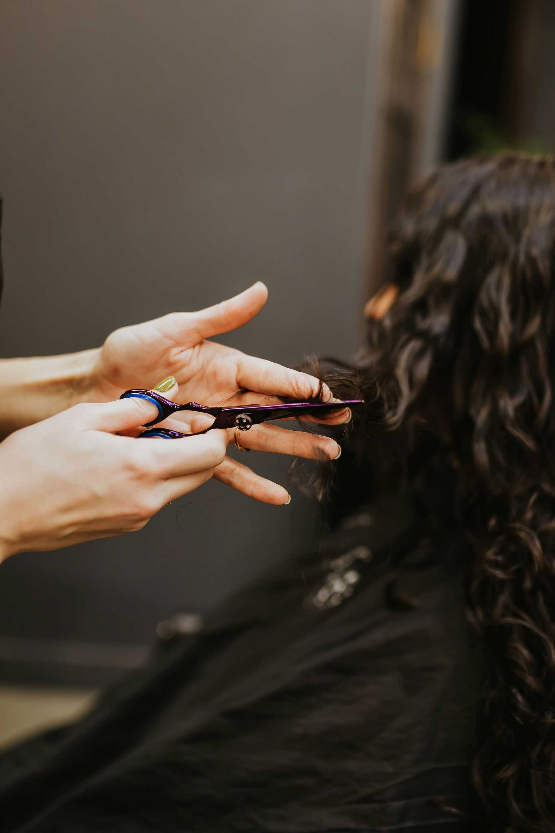 Hairdresser trimming a client's long, curly hair in a salon.